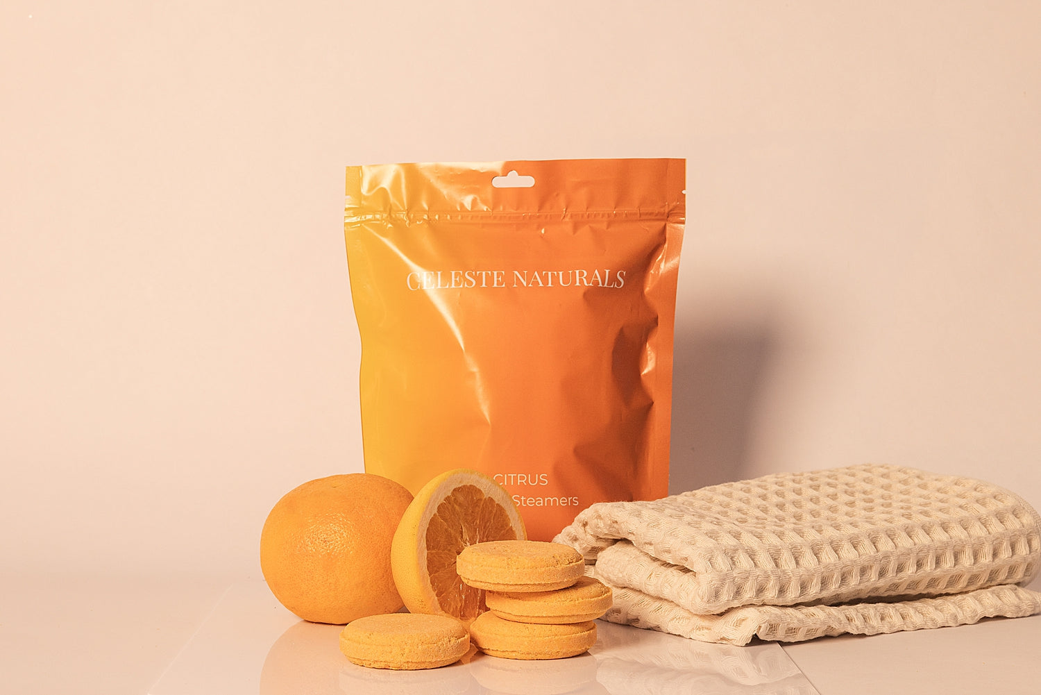 CELESTE NATURALS CITRUS shower steamer bag and tablets with orange slices and a towel on a beige background