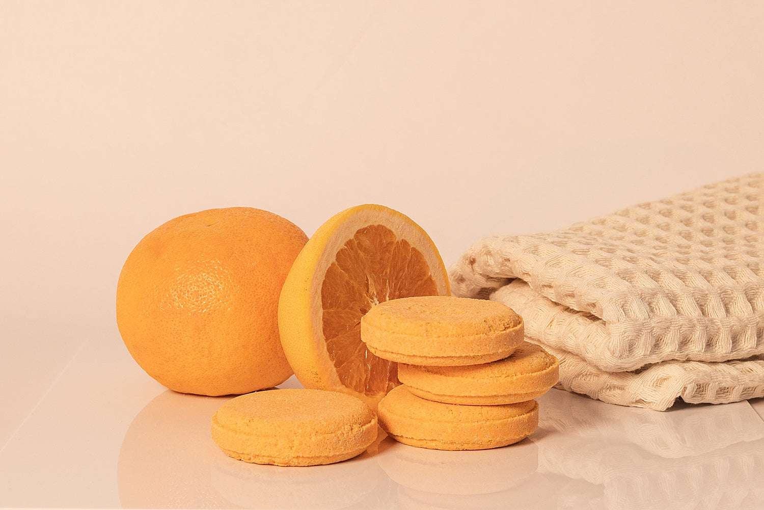 Stack of CELESTE NATURALS CITRUS shower steamer tablets and orange slices with a woven towel on a beige background