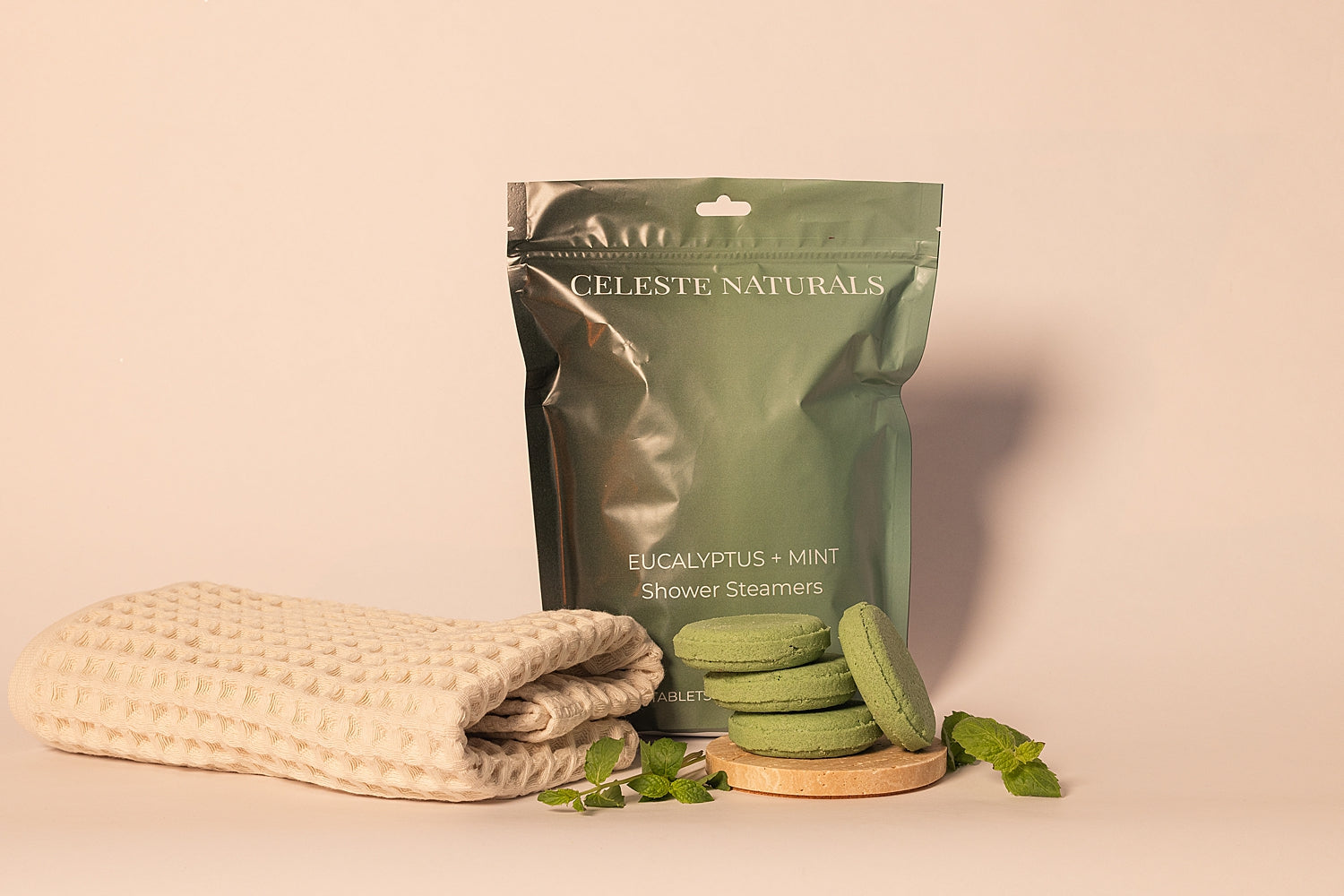 CELESTE NATURALS EUCALYPTUS + MINT shower steamers with packaging and a towel on a beige background