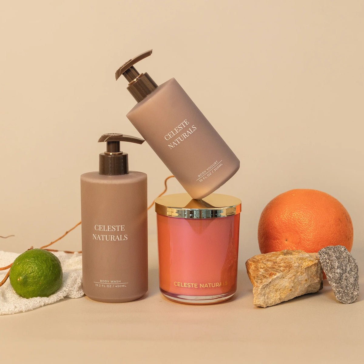Celeste Naturals Grapefruit + Bergamot Body Yogurt bottle, Body Wash bottle, and candle in pink vessel with gold lid.