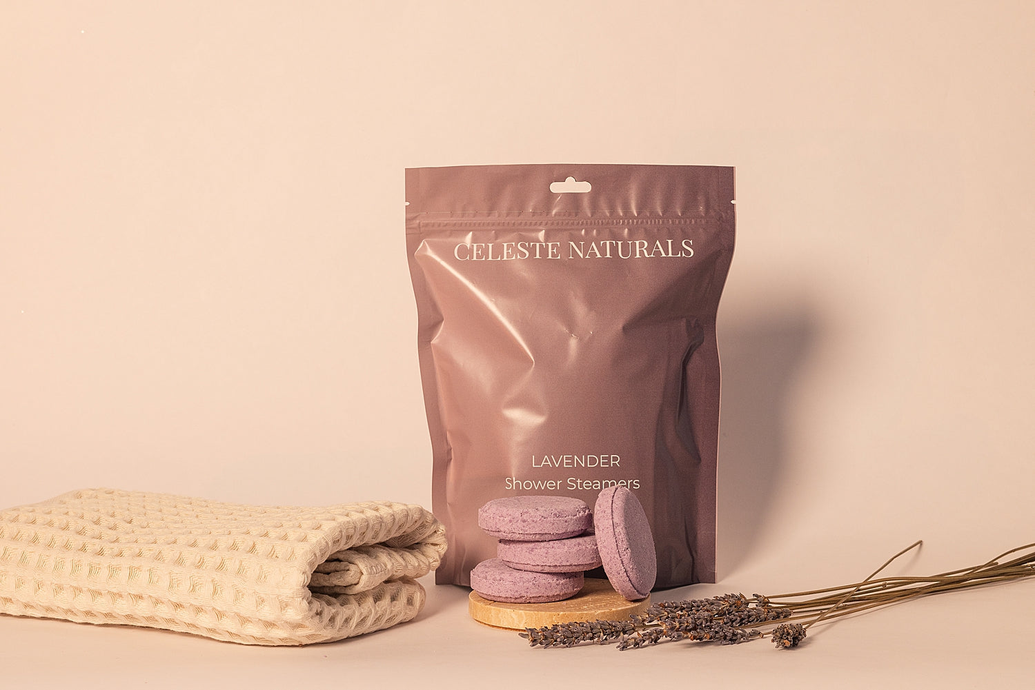 Package of CELESTE NATURALS LAVENDER shower steamers with a textured towel and lavender flowers on a beige background
