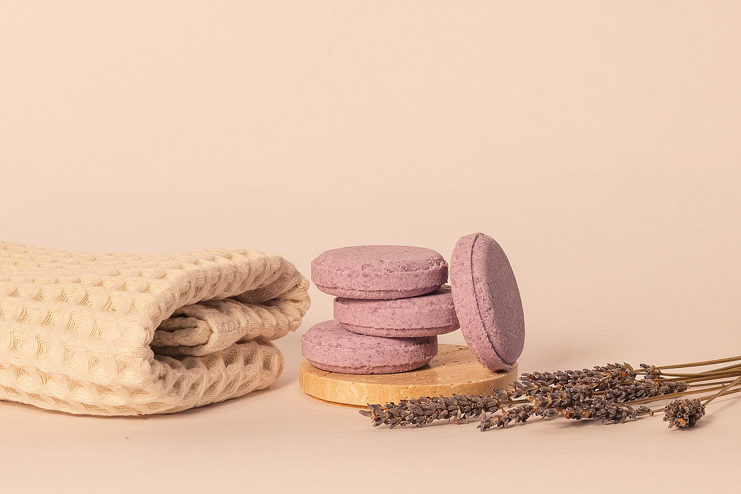 CELESTE NATURALS LAVENDER shower steamer tablets on a wooden stand with a beige towel and lavender flowers on a beige background