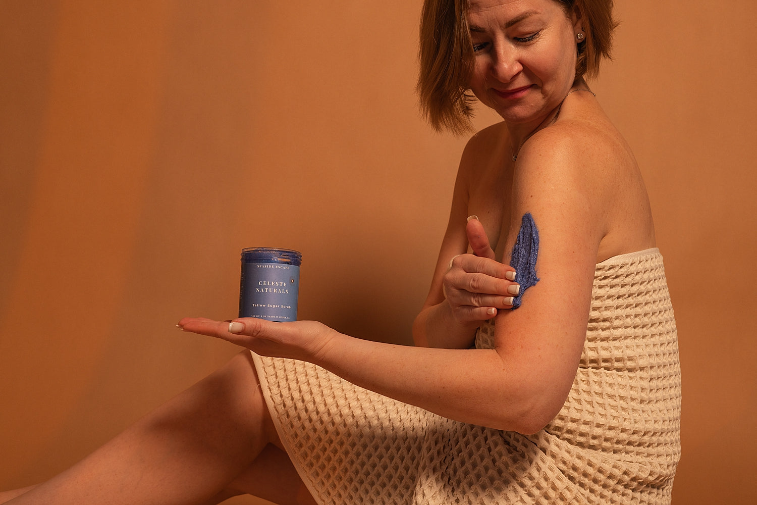 Woman applying CELESTE NATURALS SEASIDE ESCAPE Sugar Scrub to her arm.