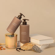 Celeste Naturals Vanilla + Almond Body Wash, Body Yogurt, and candle in beige iridescent vessel with gold lid.