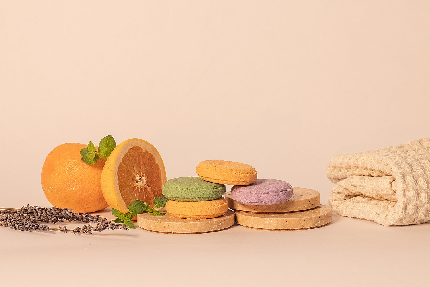 Stack of CELETE NATURALS shower steamers on wooden stands with oranges, lavender, and a towel on a beige background